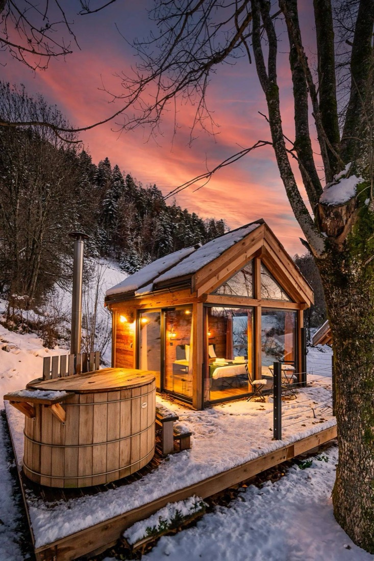Cabane vitrée avec bain nordique sous la neige au coucher du soleil